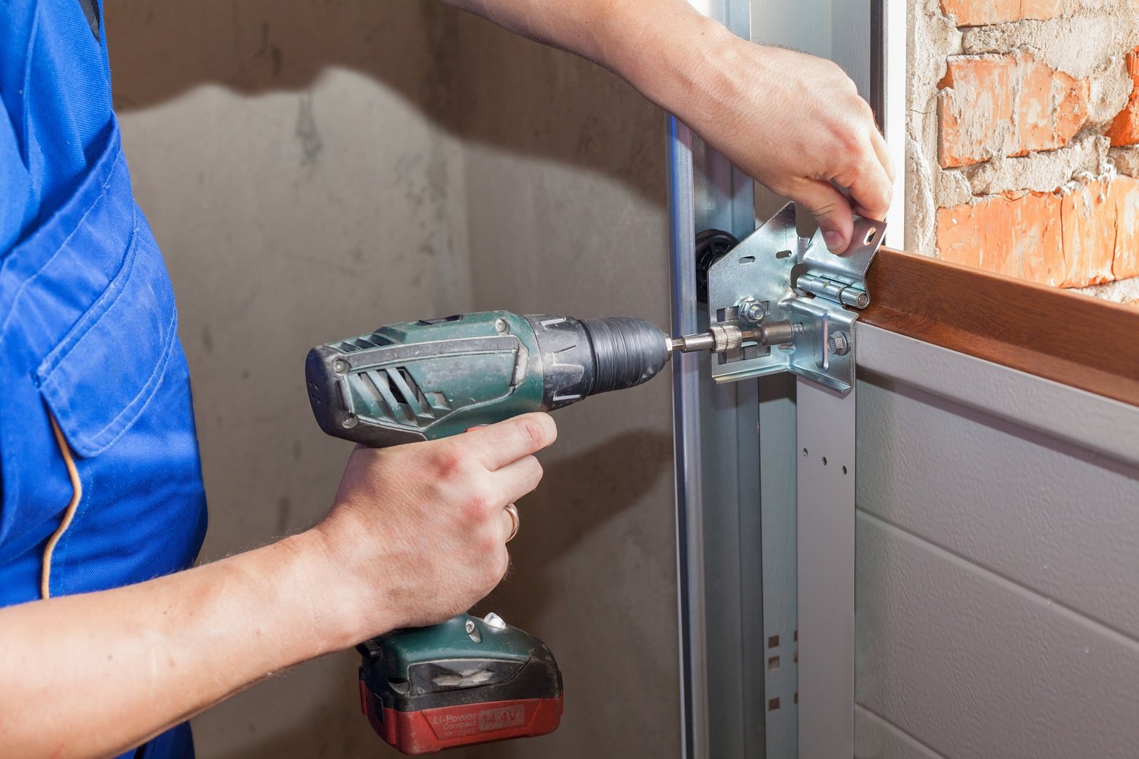Garage doors installation.Worker installing lifting system in metal profil with screwdriver